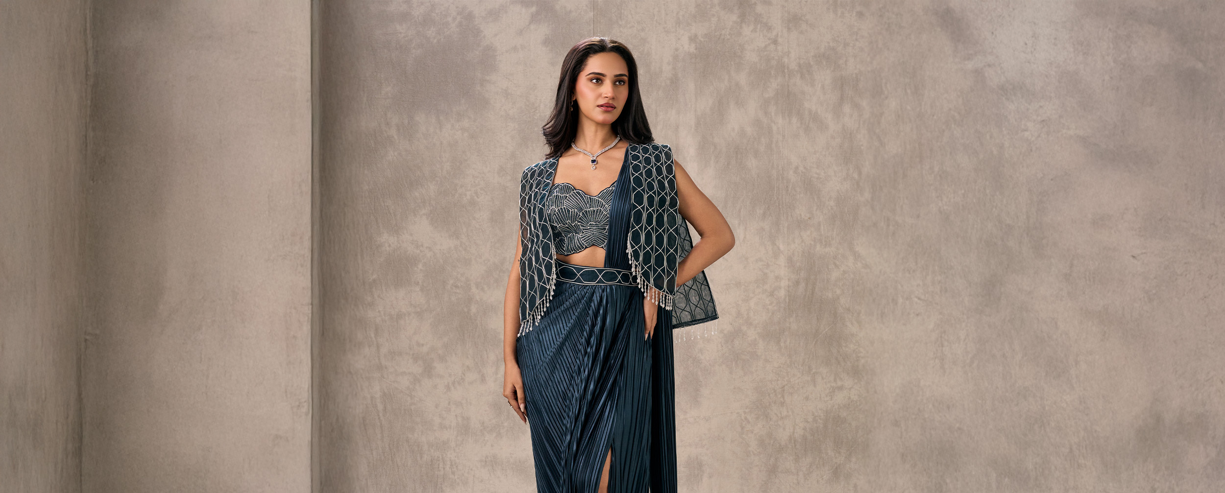 Woman in a pleated navy blue saree with a silver embroidered bustier and geometric patterned cape.