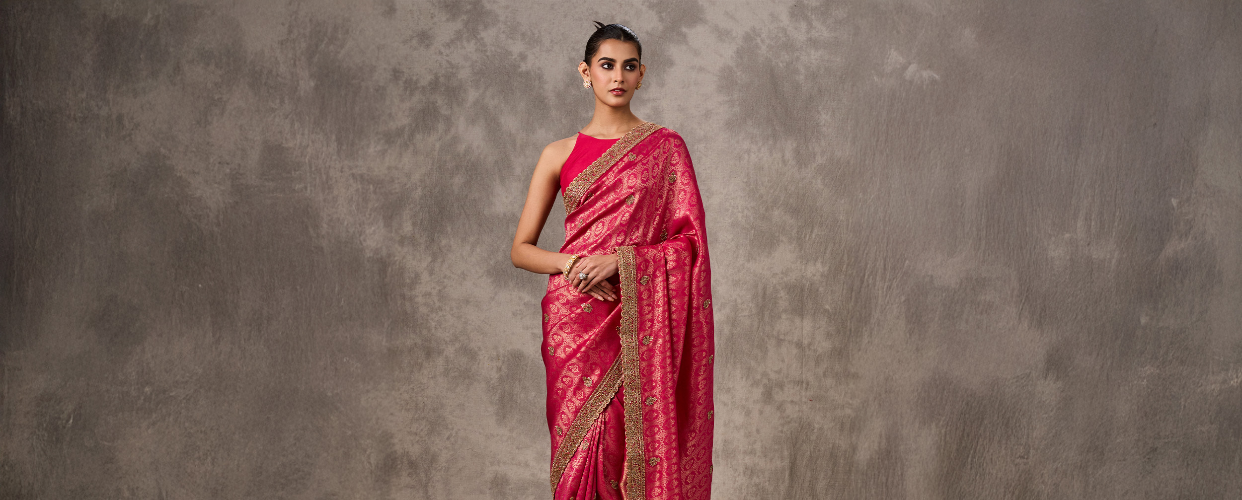 Woman in a bright pink Banarasi silk saree with a gold woven border and a matching pink halter-neck blouse.