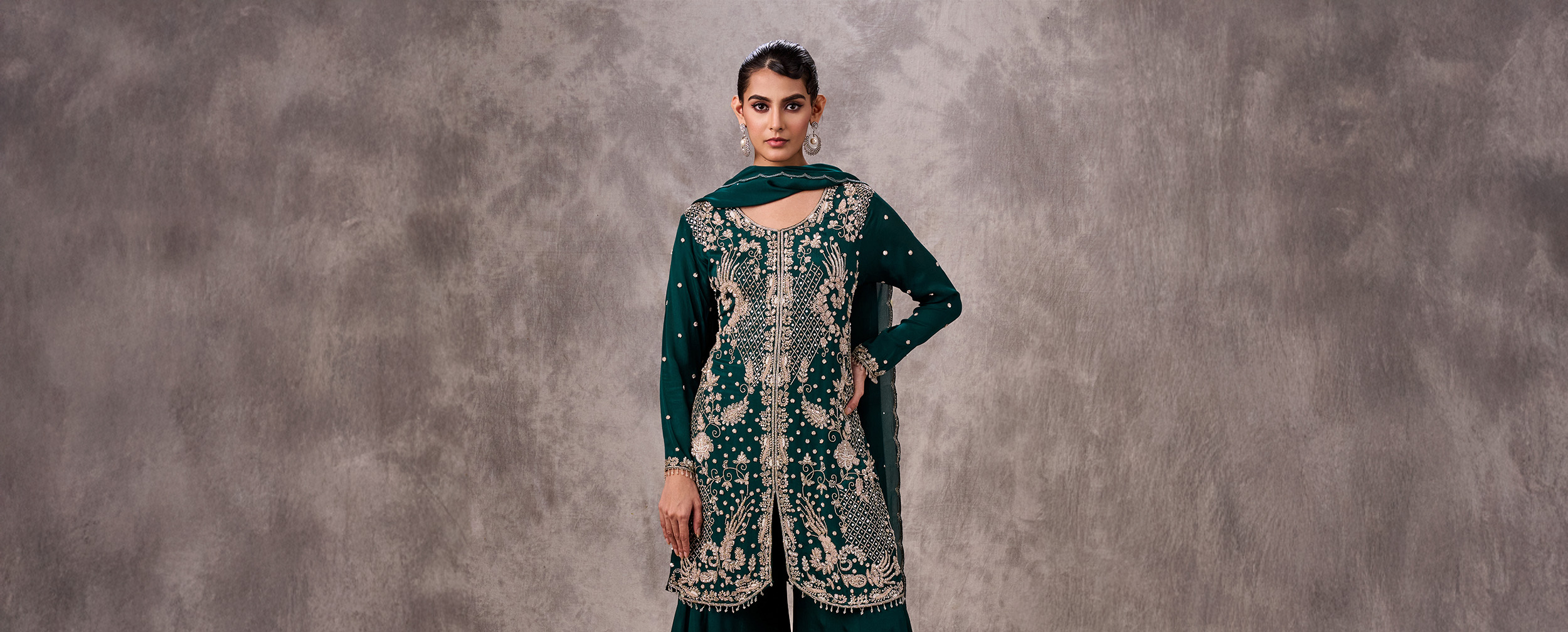 Woman in a heavily embroidered dark green Gharara suit with a sheer dupatta, showcasing an intricate festive outfit.