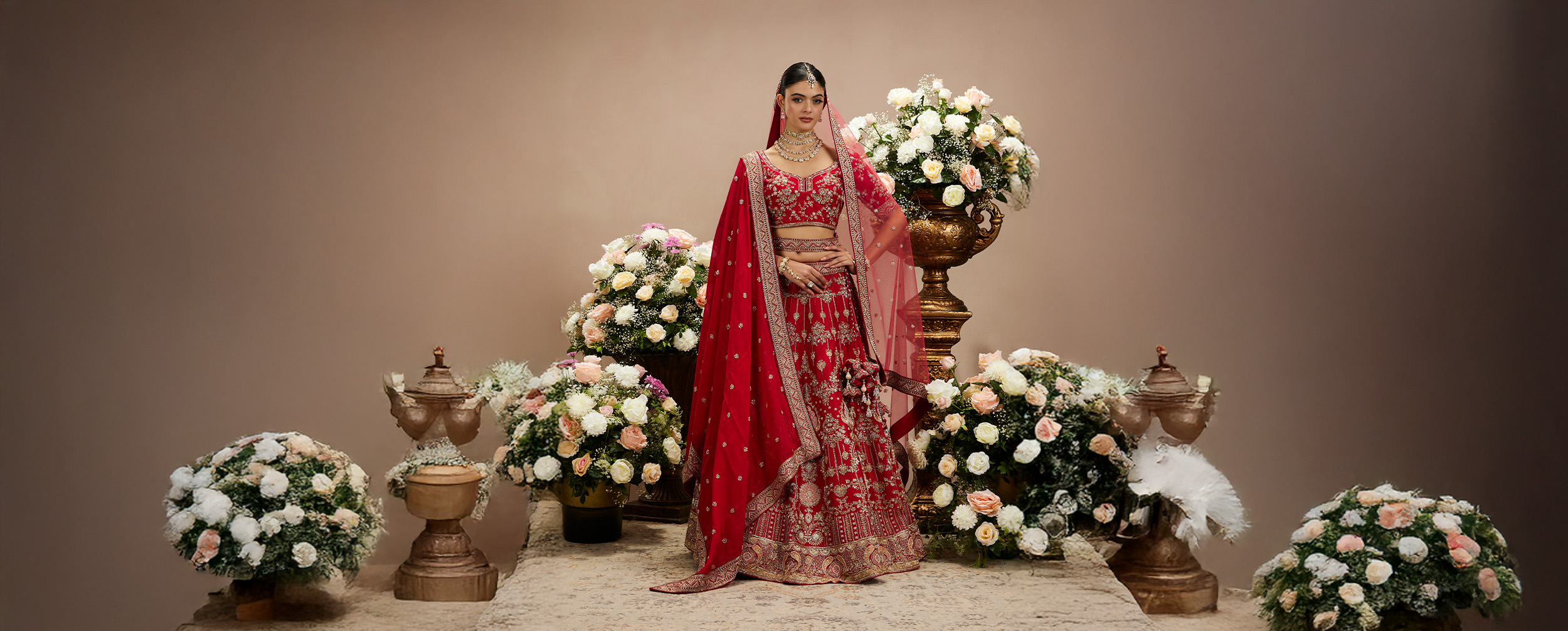  Red and gold bridal lehenga with intricate embroidery and cancan skirt, posing in an ornate archway.