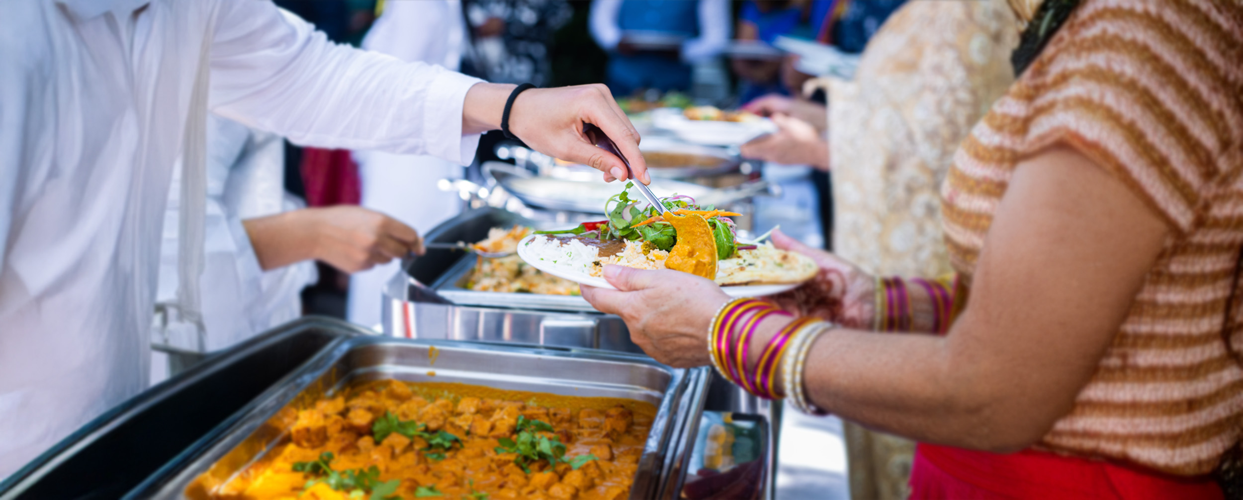 Close-up of a wedding guest serving themselves from a buffet with Indian food, including curry, rice, and naan.