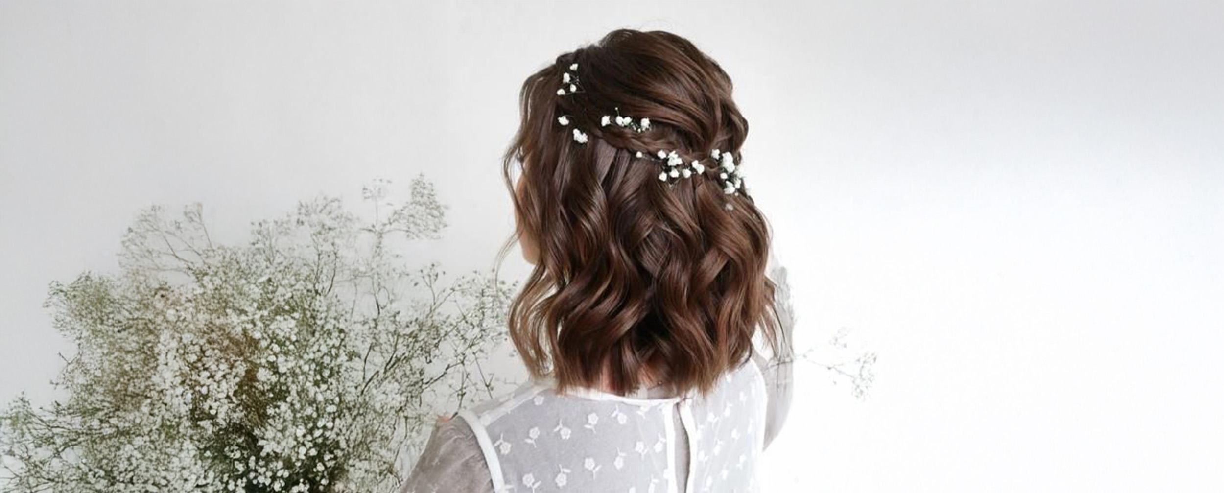 Woman showcasing a wavy brown bob hairstyle with a braided crown accented by delicate baby's breath flowers.
