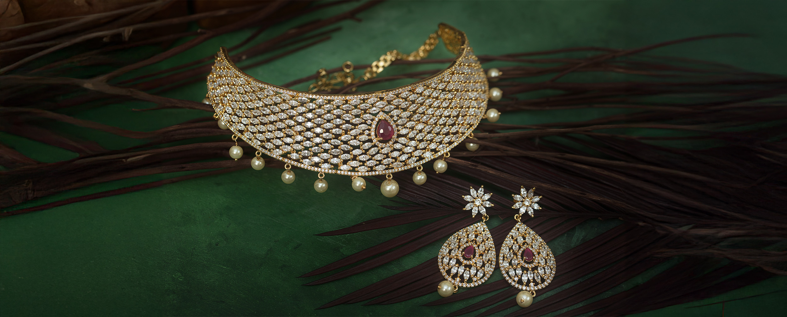 Gold-plated bridal choker necklace and matching tear-drop earrings featuring white stones and a central ruby accent.