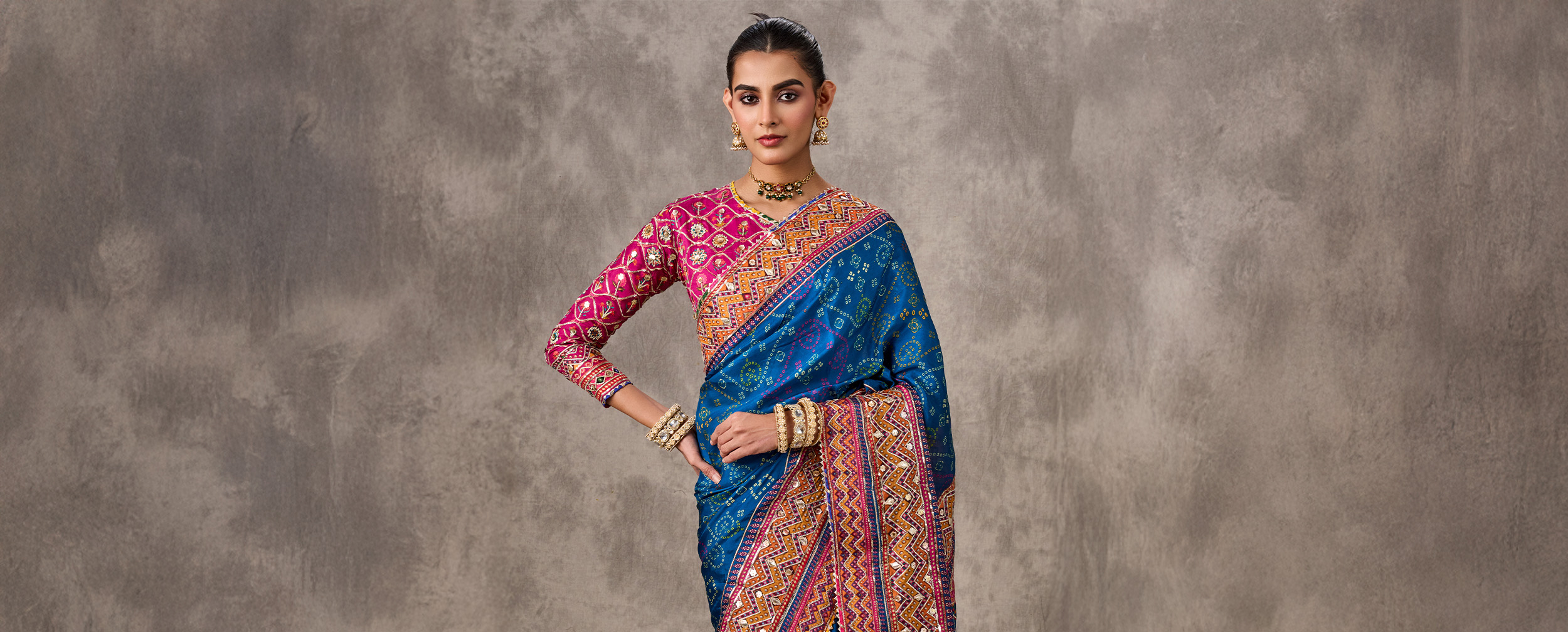 Woman modeling a vibrant blue Bandhani saree with mirror work, paired with a bright pink embroidered blouse for color contrast.